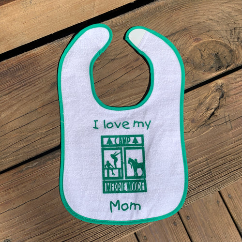 White baby bib with green Merrie-Woode logo, which shoes a horse, its rider, and two girls on a dock. The bib had a light green outline.