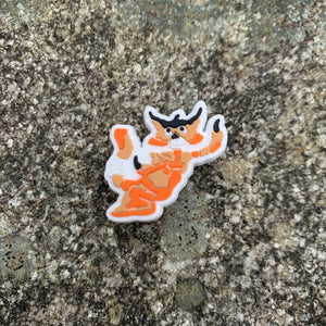 1 inch tall, rubber Croc charm of the orange/tan colored Tajar - forest creature who is part tiger, badger, and jaguar. The Tajar charm is sitting on grey, speckled stone.