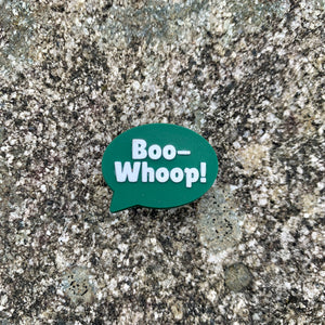 1 inch tall, rubber Croc charm of a dark green speech bubble that says "Boo-Whoop!" sitting on grey, speckled stone.