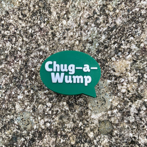 1 inch tall, rubber Croc charm of a dark green speech bubble that says "Chug-a-Wump" sitting on grey, speckled stone.