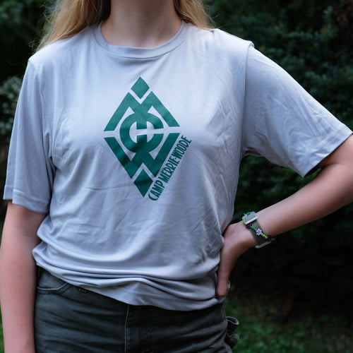 Blonde girl standing by a tree wearing a grey, dry fit material t-shirt that has the Merrie-Woode diamond logo across the front. 