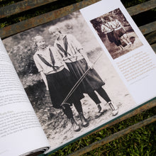 Load image into Gallery viewer, Page of the Merrie-Woode centennial book, showing a large picture of founders Dammie Day and Mary Turk, wearing gray middies, green ties, green bloomers, and bandanas on their heads.

