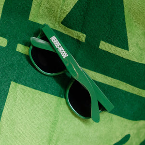 Light green framed sunglasses, that say "Merrie-Woode" on the side. Glasses are sitting on a lime green beach towel.